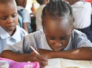 A young girl writing in a book while another looks on