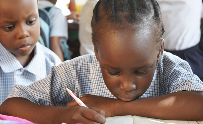 A young girl writing in a book while another looks on